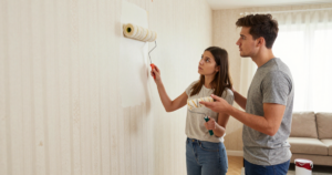 couple painting over wallpaper with roller